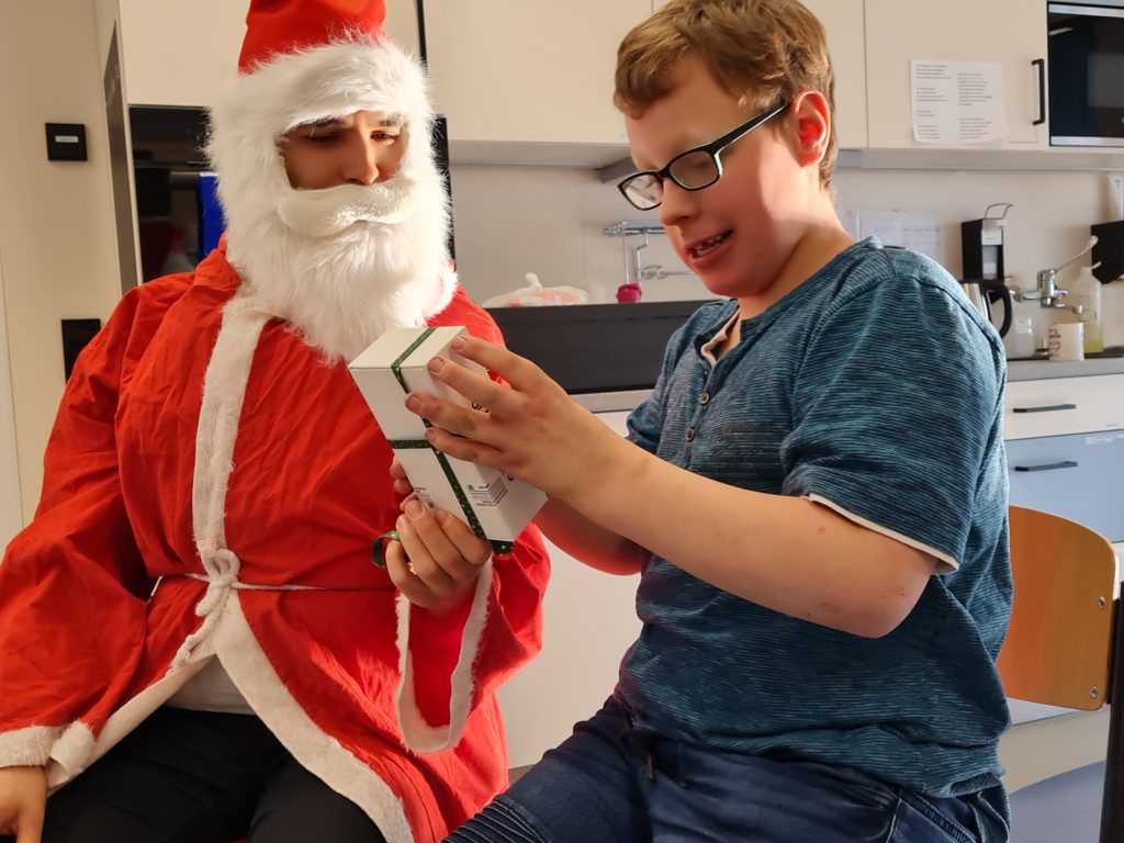 Ein Schüler erhält vom Weihnachtsmann ein Handy in Originalverpackung und mit einer Schleife.