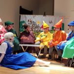 Schauspiel-Nachwuchs auf der Bühne: Sieben Zwerge in knallbunten Kostümen mit Zipfelmützen und im Vordergrund eine Prinzessin. Alle tragen ein Headset-Mikrofon.