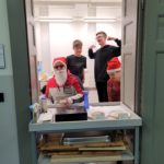 Vier Schüler haben Spaß beim Verkauf von Waffeln und Kaffee. Manche tragen eine Weihnachtsmütze.