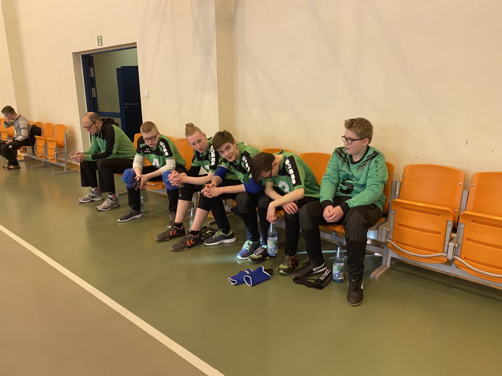 Die Chemnitzer Mannschaft sitzt  mit Herrn Theiß in der Turnhalle auf der Wartebank.
