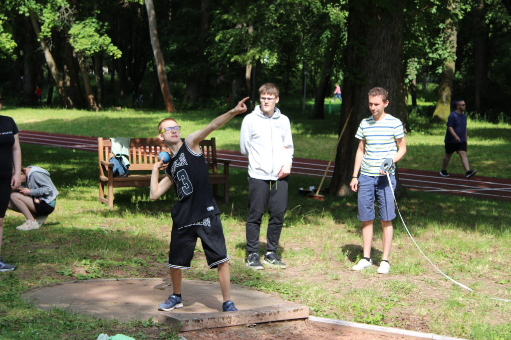 Ein Schüler beim Kugelstoßen. Die Helfer stehen bereit, um die erzielte Leistung auszumessen.