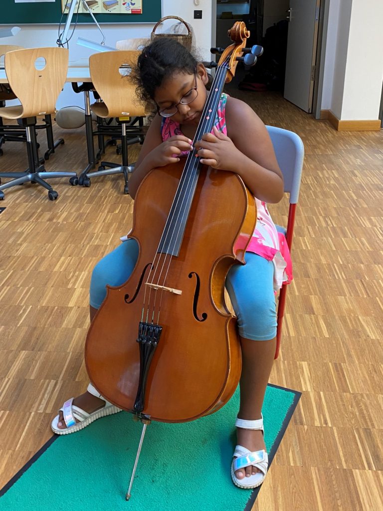 Ein Mädchen macht sich mit den vier Saiten eines Cellos vertraut.