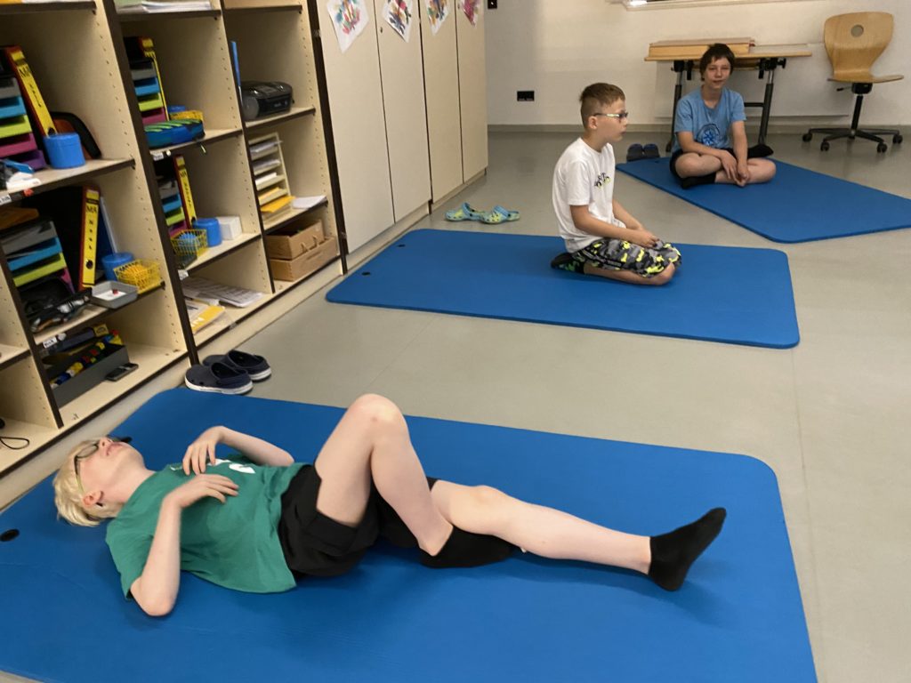 Drei Jungs haben im Klassenraum Yogamatten ausgebreitet und entspannen sich.