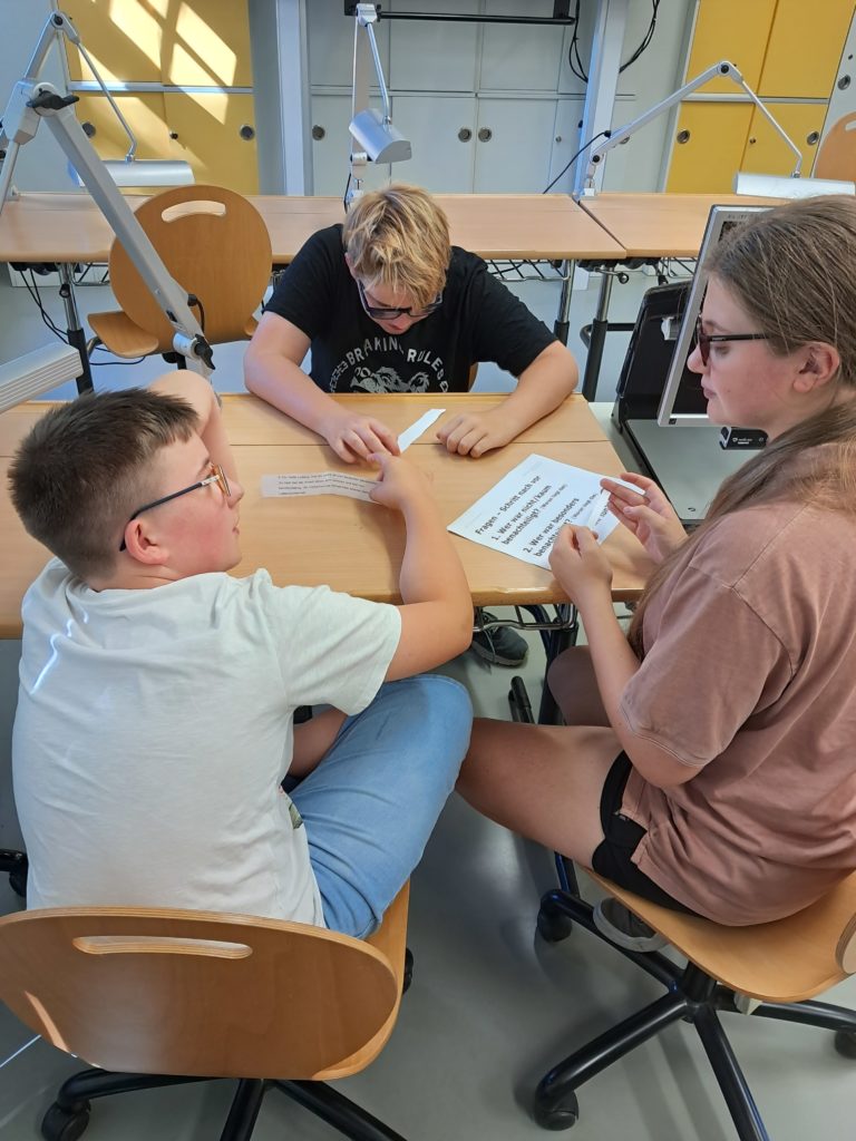 Eine Gruppe aus 3 Schülern diskutiert mit Fragezetteln über Privilegien und Benachteiligungen.