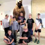Klassenfoto mit 8 Kindern der Klasse 7a. Im Hintergrund der Gruppe steht ein ausgestopfter Braunbär. Er ist beinahe doppelt so groß wie die Menschen.