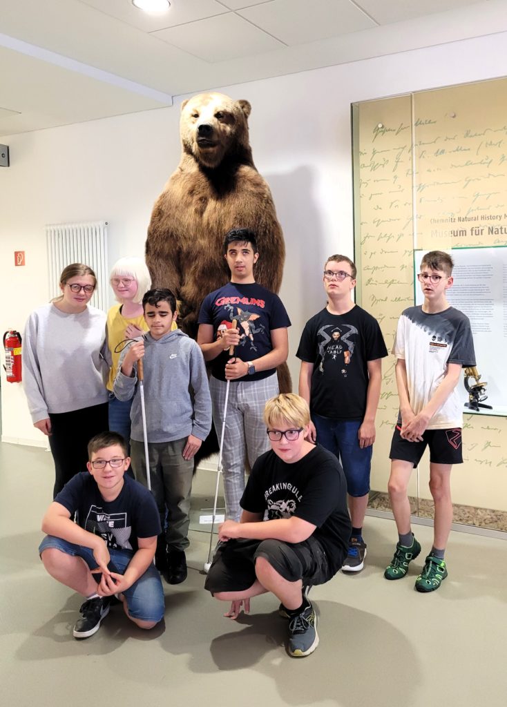 Klassenfoto mit 8 Kindern der Klasse 7a. Im Hintergrund der Gruppe steht ein ausgestopfter Braunbär. Er ist beinahe doppelt so groß wie die Menschen.