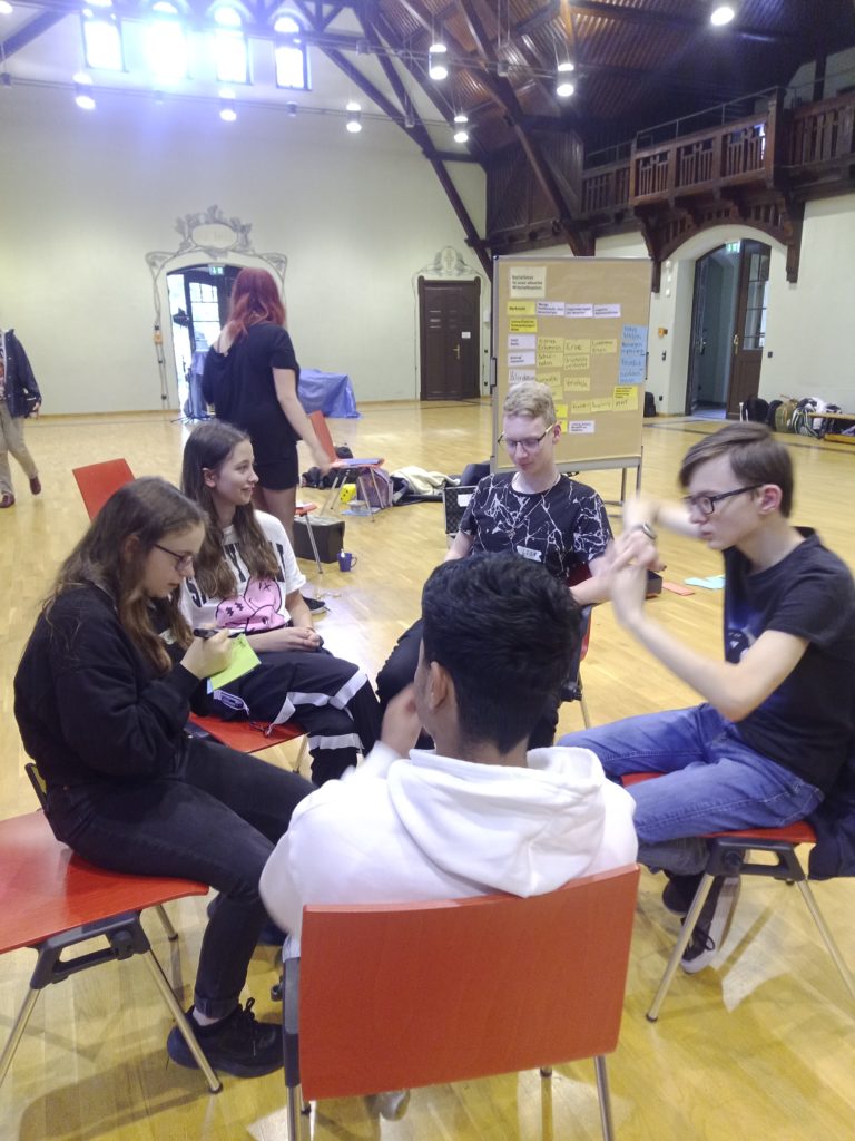 Eine Gruppe Schüler diskutiert mit ernster Miene. Anakin gestikuliert dabei mit seinen Armen.
