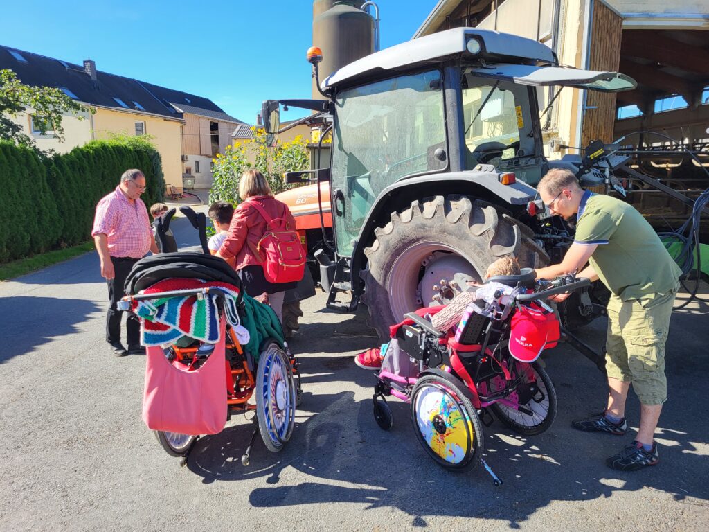 Schüler in Rollstühlen stehen vor einem Traktor. Es ist sonniges Wetter.