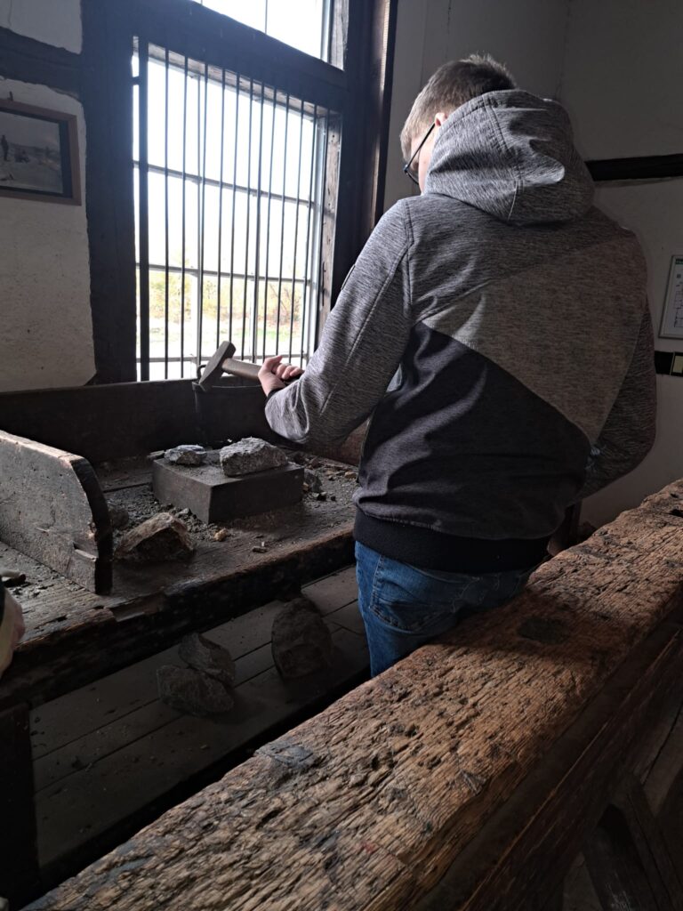 Ein Schüler hat einen Hammer in der Hand und bearbeitet damit ein Gestein.
