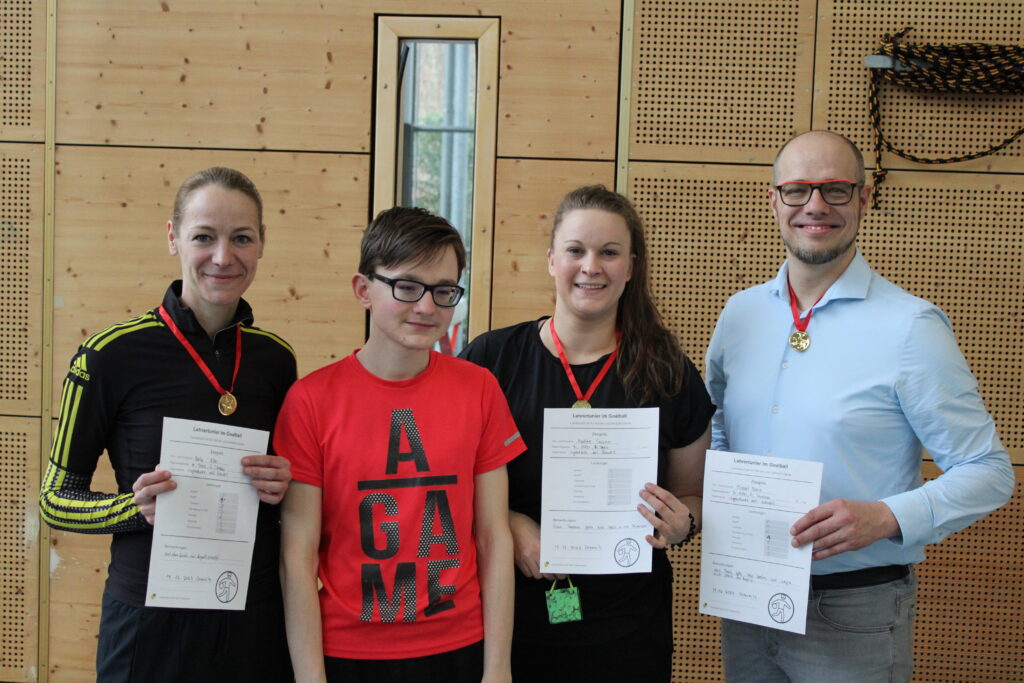 Das erfolgreiche Lehrerteam posiert mit ihren Medaillen und Zeugnissen in der Hand.
