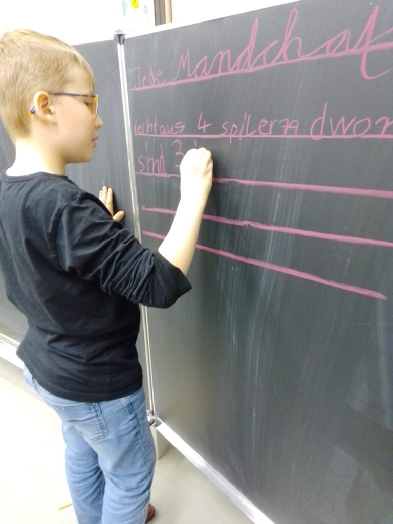 Ein Schüler notiert eine Spielidee mit Kreide an der Tafel.