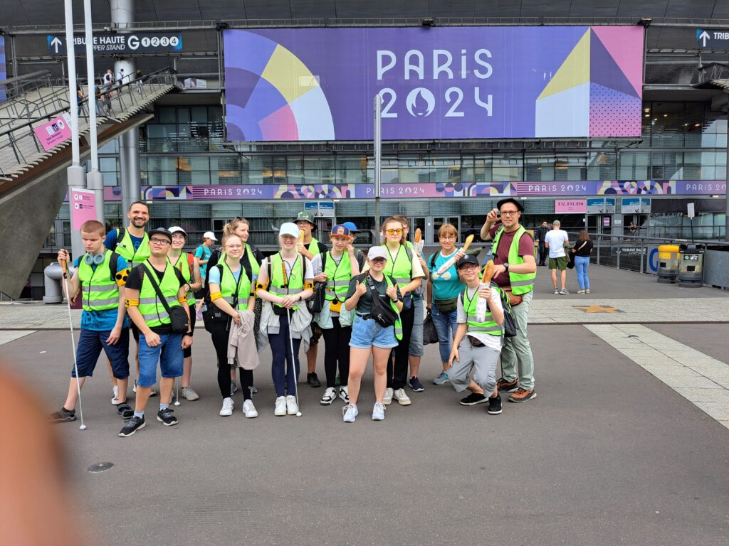 Ein Gruppenfoto der Reisegruppe vor dem Eingang des Stade de France. Im Hintergrund ein Banner mit der großen Aufschrift Paris 2024.