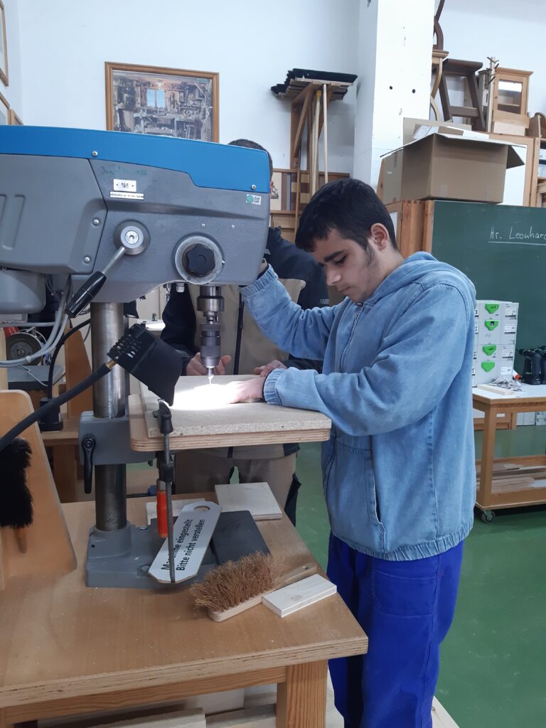 Ein Schüler bearbeitet Holz mit einer großen Standbohrmaschine