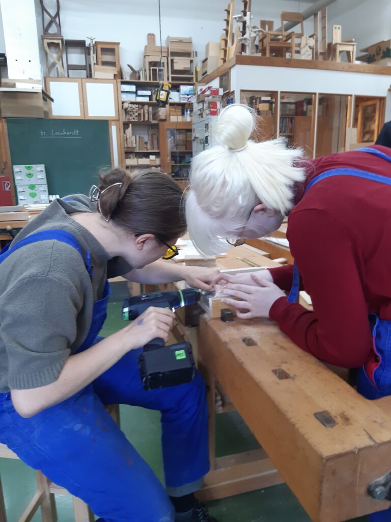 Zwei Schülerinnen bearbeiten Holz mit einer Handbohrmaschine