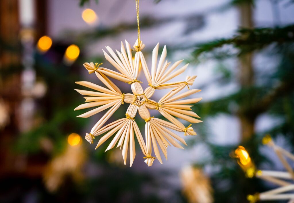 Ein Strohstern in Großaufnahme. Der Hintergrund ist verschwommen. Es sieht aus, als würde der Strohstern an einem Weihnachtsbaum hängen.