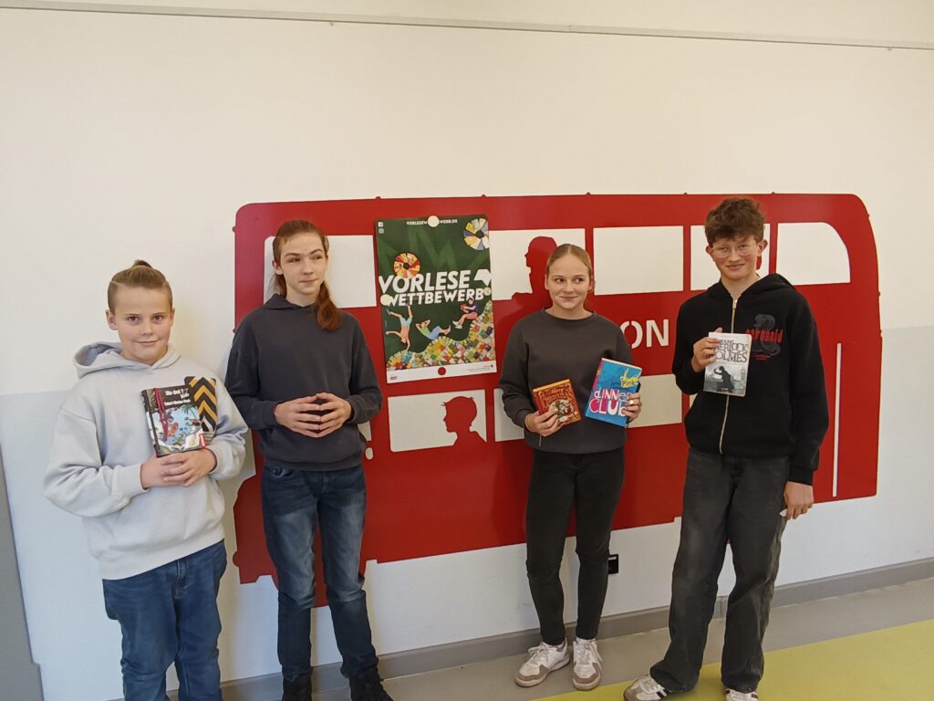 Alle Teilnehmenden stehen mit ihren Büchern vor dem Plakat "Vorlesewettbewerb".