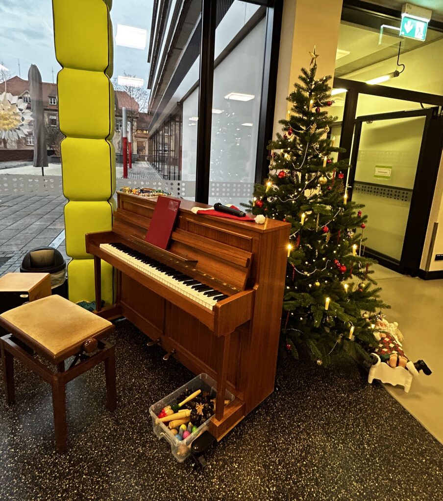 Ein Klavier, hinter dem ein weihnachtlich geschmückter Tannenbaum zu sehen ist
