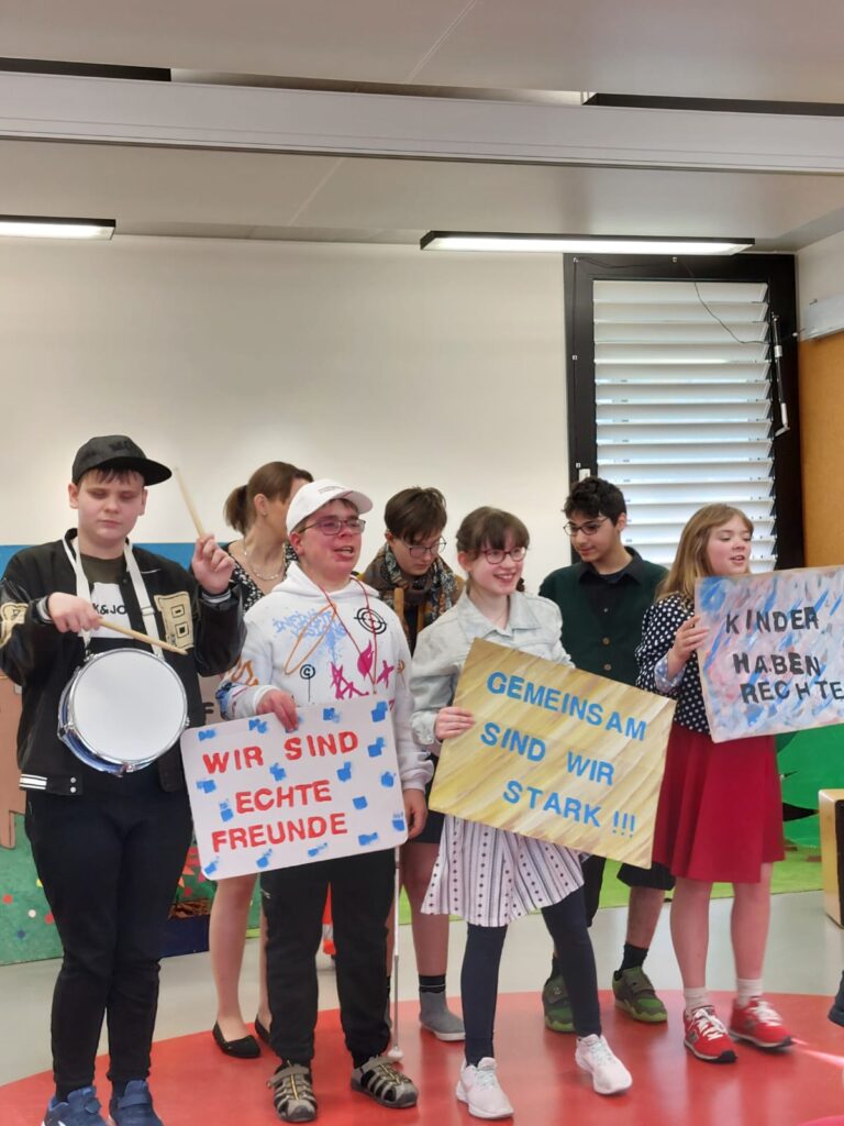 Gruppenfoto der Teilnehmenden, sie haben Plakate in der Hand: "Wir sind echte Freunde." "Gemeinsam sind wir stark." "Kinder haben Rechte".