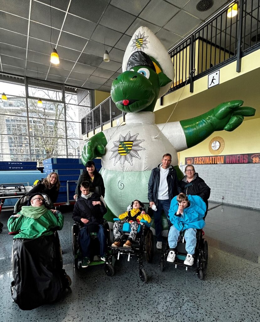 Personen neben dem Polizeimaskotchen Poldi (grüner Drache im weißen Anzug mit Polizeizeichen).