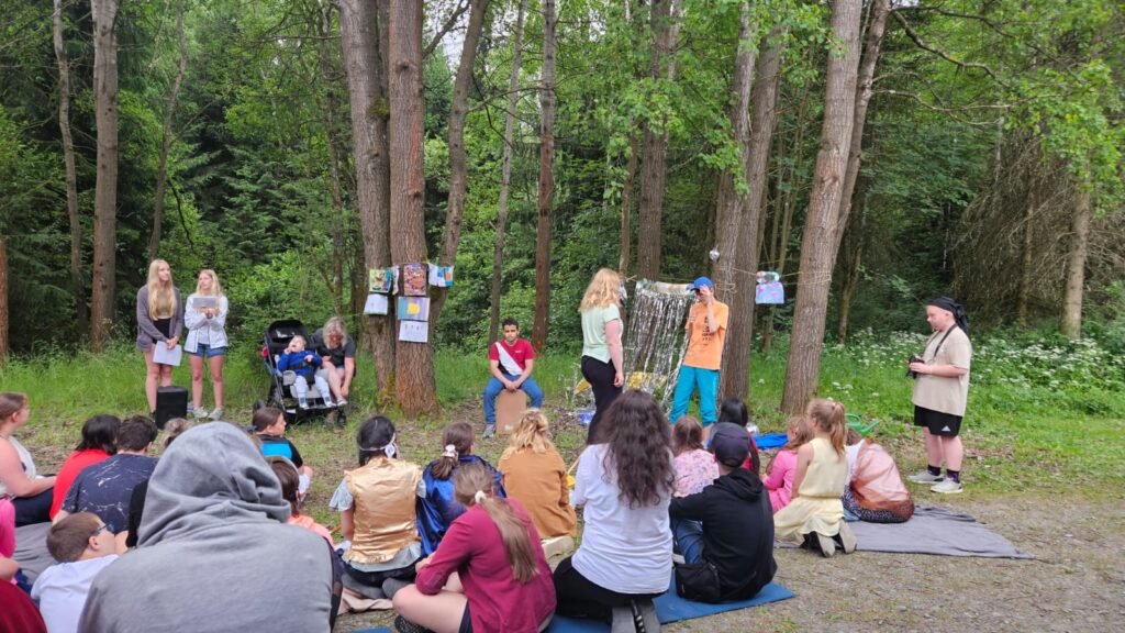 eine grupe schülern spielen theater auf der wiese zuschauer sitzen auf der decke.