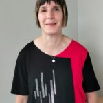 Birgit mit kurzen braunee Haaren und einem schwarz-rotem T-Shirt lächelt freundlich