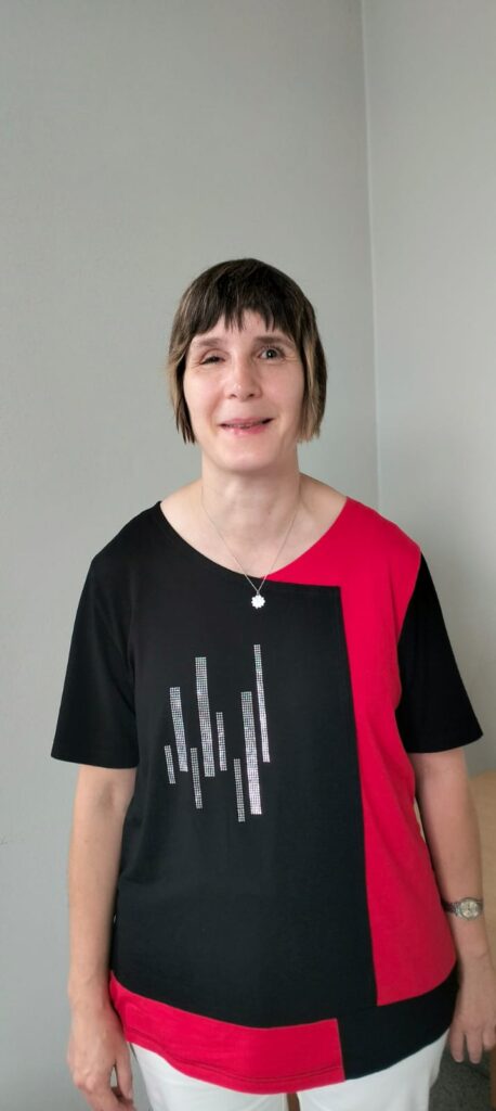 Birgit mit kurzen braunee Haaren und einem schwarz-rotem T-Shirt lächelt freundlich