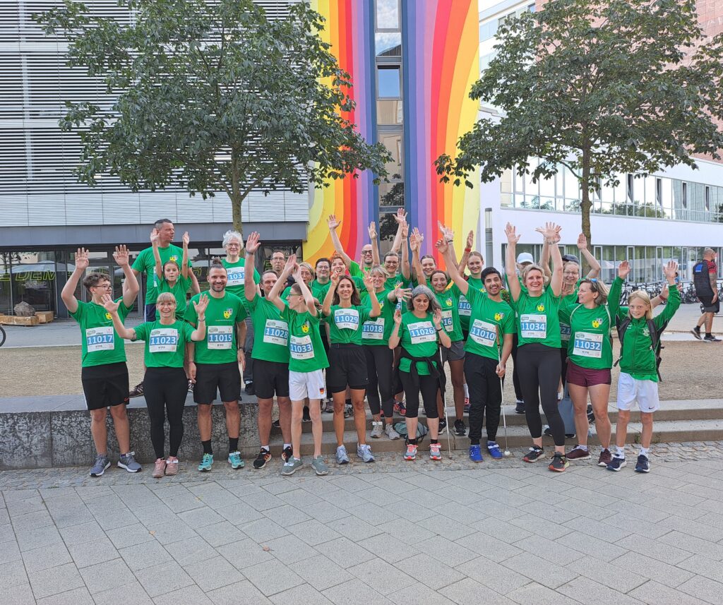 Gruppenfoto aller Läuferinnen und Läufer. Alle tragen grüne Shirts, einige haben die Arme noch oben geworfen.