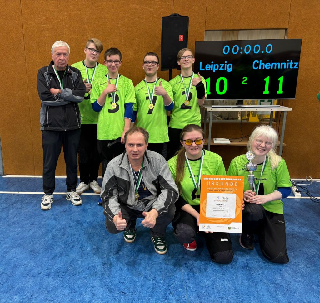 Siegerfoto mit allen 6 Spielern und den 2 Trainern. Auf der Anzeigetafel steht es 11:10 für Chemnitz. Eine Spielerin hat den Pokal in der Hand. Dazu tragen alle eine Medaille.