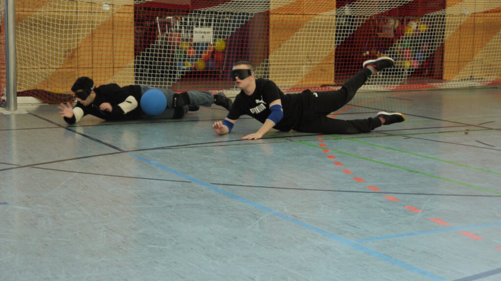 zwei Schüler die auf den Boden liegen und Goalball spielen
