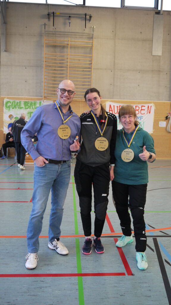 hier sind drei Lehrer zu sehen mit einer Goldmedallie aus Plastik 