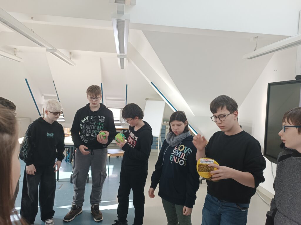Die Teilnehmenden stehen im Kreis, drei Schüler halten einen Anti-Stress-Ball in der Hand