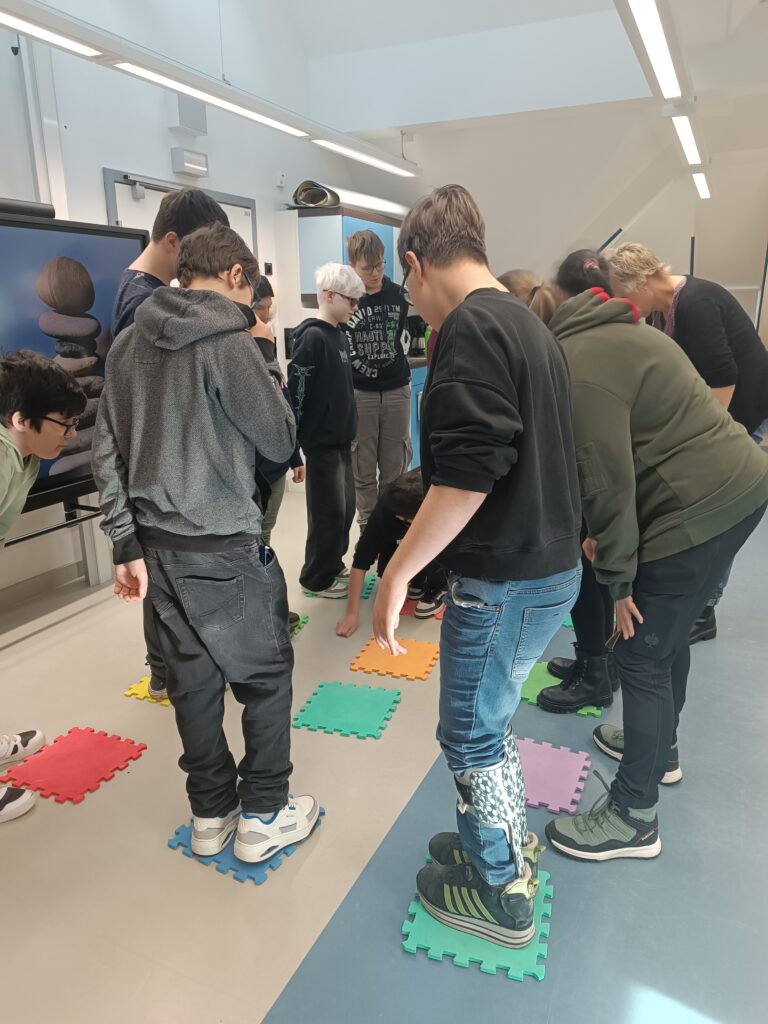 Die Teilnehmenden stehen auf kleinen Stücken einer Puzzlematte, welche im Raum verteilt sind