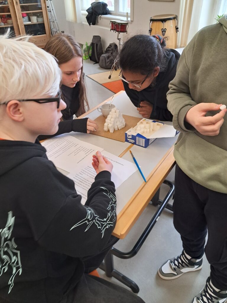 3 Schüler basteln aus Zuckerstücken einen Eisberg