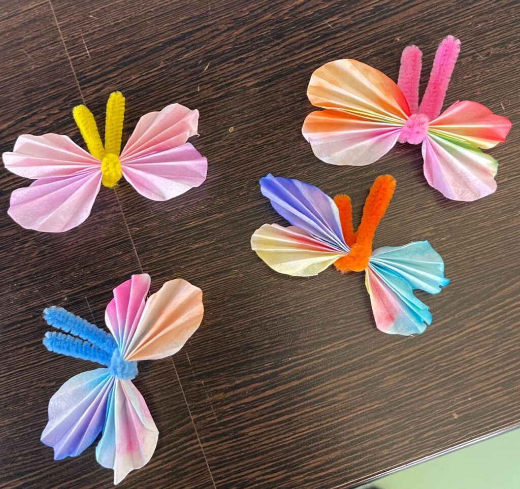 vier selbst gebastelte buntpapier Schmetterlinge die auf einem Tisch liegen