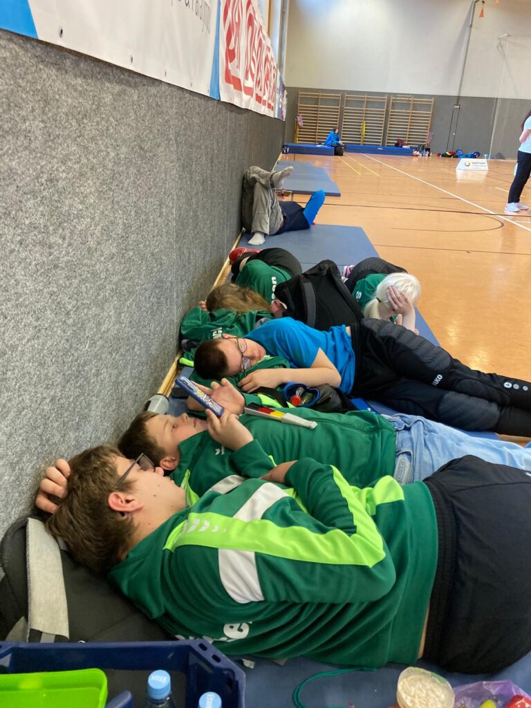5 Schülerinnen und Schüler liegen auf Matten in einer Turnhalle und ruhen sich aus.