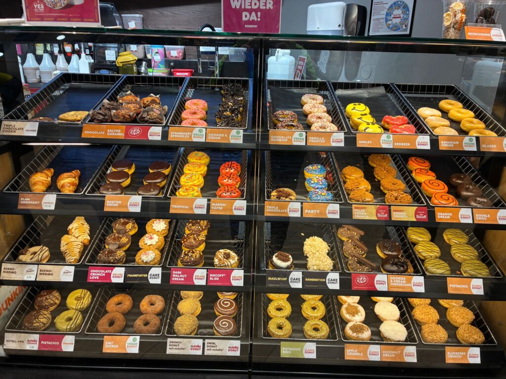 Die Auslage eines Donutladens mit vielen verschiedenen Donats in verschiedenen Farben.
