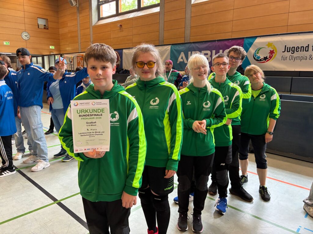 Das Team steht in der grünen Teamjacke hintereinander in der Reihe. Der erste Schüler hält die Urkunde für Platz 4 in der Hand.