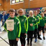 Das Team steht in der grünen Teamjacke hintereinander in der Reihe. Der erste Schüler hält die Urkunde für Platz 4 in der Hand.