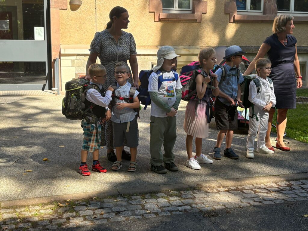Klasse 1a stehen vorm dem Haus 16 sind 6 Schüler ( 5 jungs und 1 Mädchen ) und 2 Lehrerin