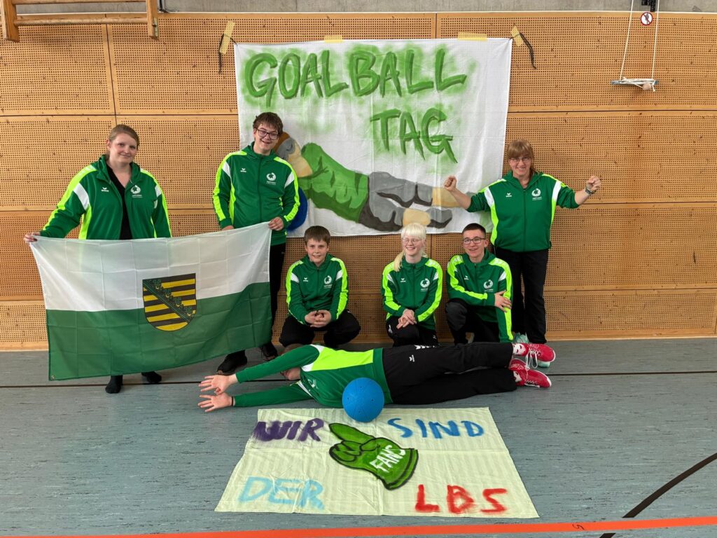 Gruppenfoto der Schulmannschaft, mit der Flagge des Freistaates Sachsen und 2 Bannern: "Goalballtag" sowie "Wir sind Fans der LBS"