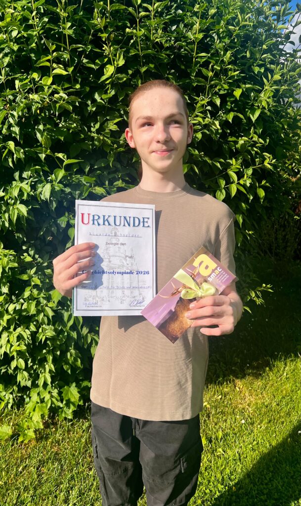 der Schüler Ricardo hält eine Urkunde in der Hand mit dem 1. Platz und einem Gutschein